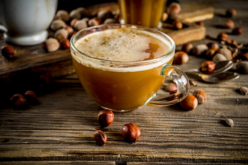 Homemade hazelnut coffee latte or cappuccino, rustic wooden background with hazelnuts, three coffee cups copy space