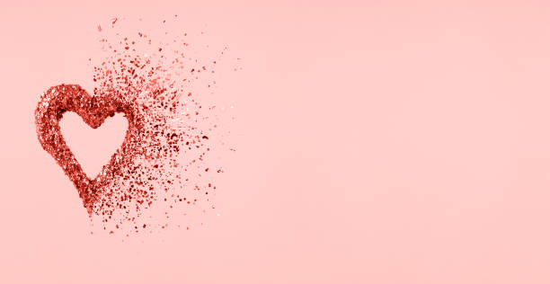 istock Glitter heart dissolving into pieces on pink background.  Valentines day, broken heart and love emergence concept. Coral color 1095101032