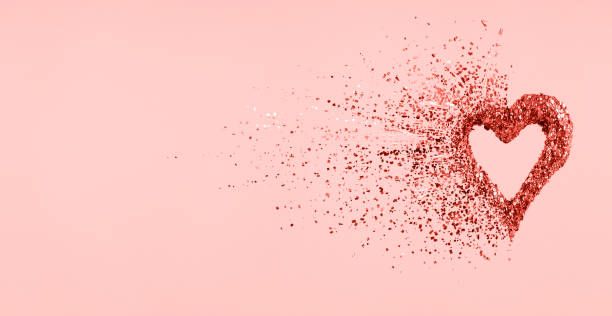istock Glitter heart dissolving into pieces on pink background.  Valentines day, broken heart and love emergence concept. Coral color 1095101036
