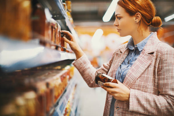 I simply adore Sun-dried tomatoes. Young woman holding a jar of Sun-dried tomatoes in supermarket. She's searching for specific manufacturer. grocery shelf cans stock pictures, royalty-free photos & images