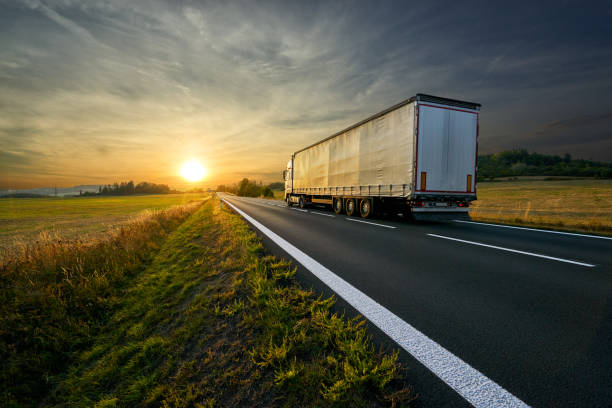 lkw auf einer asphaltierten straße in richtung sonnenuntergang in einer ländlichen gegend laufen - vanishing point summer cloud sky stock-fotos und bilder