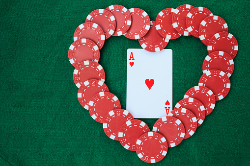 Heart made with poker chips, with an ace of hearts, on a green background table. Top view with copy space.