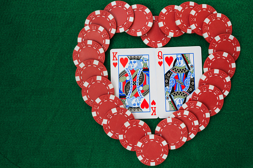 Heart made with poker chips, with king and queen of hearts, on a green background table. Top view with copy space.