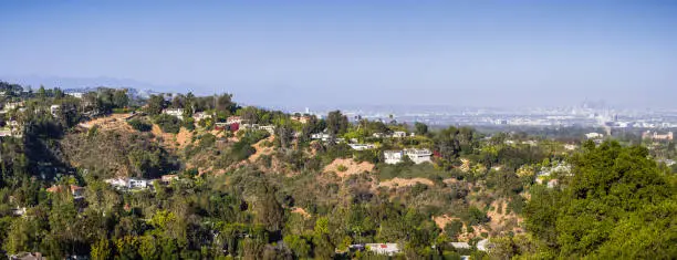 Scattered mansions on one of the hills of Bel Air neighborhood; the downtown skyscrapers visible in the background through a hazy atmosphere; Los Angeles, California