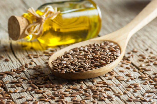 cumulo di semi di lino o semi di lino in cucchiaio e ciotola con bicchiere di olio di lino su sfondo di legno. concetto di semi di lino o di lino. fibra alimentare per semi di lino - olio semi di lino foto e immagini stock