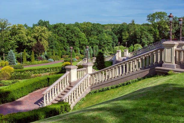 A staircase with stone railing balustrades and retro lanterns on pedestals against the backdrop of a landscape with a boxwood hedge and a forest with trees. A staircase with stone railing balustrades and retro lanterns on pedestals against the backdrop of a landscape with a boxwood hedge and a forest with trees. baluster stock pictures, royalty-free photos & images