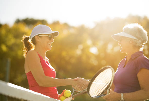 Senior women shaking hands after a friendly game of tennis on bright sunny day. Mature females shaking hands after a match on tennis court. tennis senior adult adult mature adult stock pictures, royalty-free photos & images