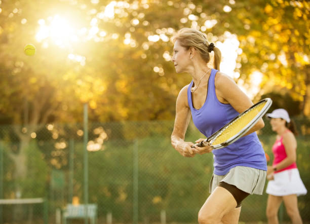 Shot of mature women playing tennis. Senior women playing a doubles tennis game on court. tennis outfit stock pictures, royalty-free photos & images