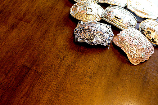 A group of trophy western belt buckles on a wood table with copy space.