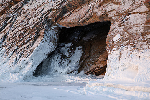 Cave entrance in textured and snow-covered rocks, view from outside, scenic winter landscape or background