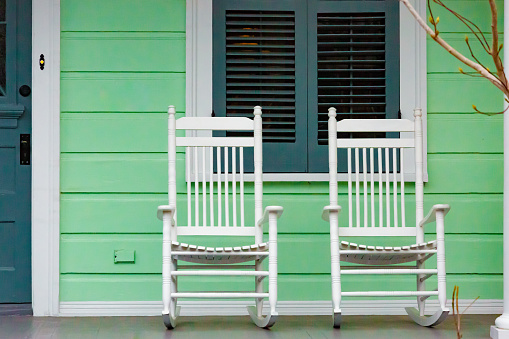Two white rocking chairs on porch of green New Orleans American Home