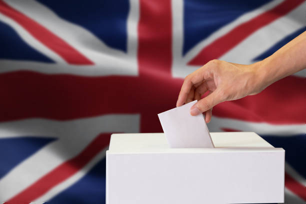 Close-up of man casting and inserting a vote and choosing and making a decision what he wants in polling box with United Kingdom or UK flag blended in background stock photo