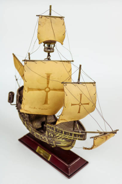 Side view of a wooden model of a three-masted sailing ship lying on wooden stands against a dark background.