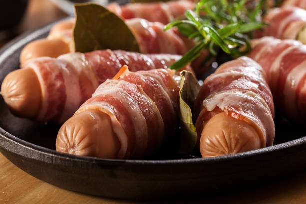 Raw mini sausages wrapped in smoked bacon stock photo