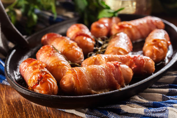 Pigs in blankets in baking dish Pigs in blankets. Mini sausages wrapped in smoked bacon in baking dish bacon wrapped stock pictures, royalty-free photos & images