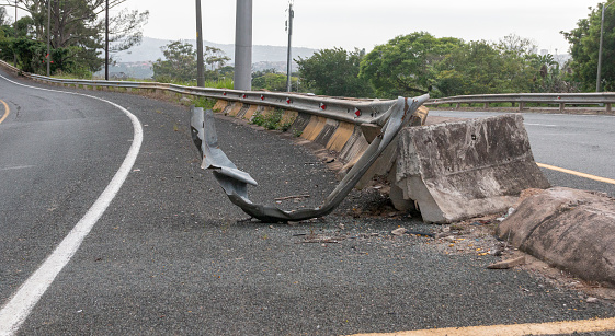 A close up view of the metal and concrete bolck barrier on the side of a freeway or motorway that has been damaged by a car or motor vehicle crashing into it