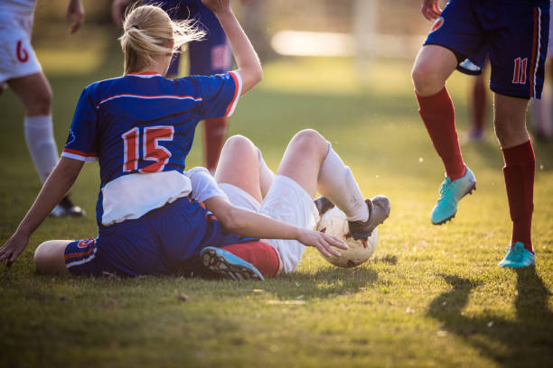Foul on women's soccer match! Female soccer players on the ground after the foul during a match on playing field. foul stock pictures, royalty-free photos & images