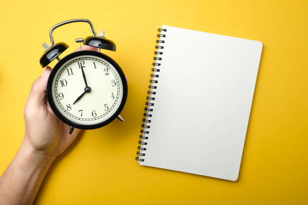 istock men holding black alarm clock in hand with blank white notebook on yellow background color 1095285878