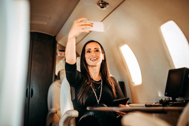 istock Rich woman smiling while using a mobile phone to take a selfie for social media while traveling on a private jet 1095289252