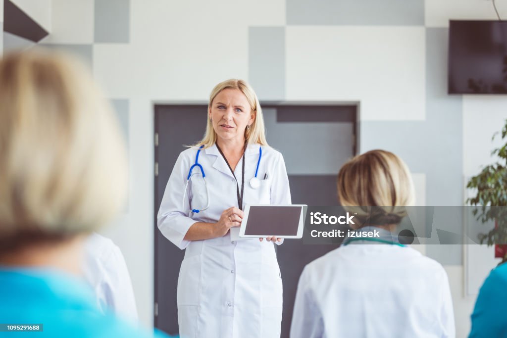 Doctor with digital tablet giving speech Mature female doctor with digital tablet giving speech to medical team. Female speaker in a seminar talking to group of women. Adult Stock Photo Doctor with digital tablet giving speech Mature female doctor with digital tablet giving speech to medical team. Female speaker in a seminar talking to group of women. Adult Stock Photo
