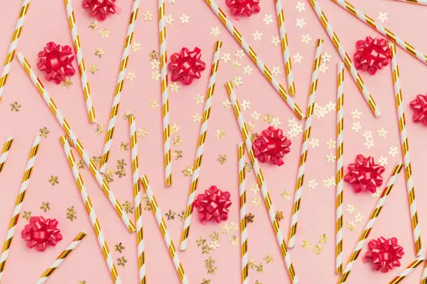Background for party. gold drinking straws, red bows, pink background. Pattern. Top view