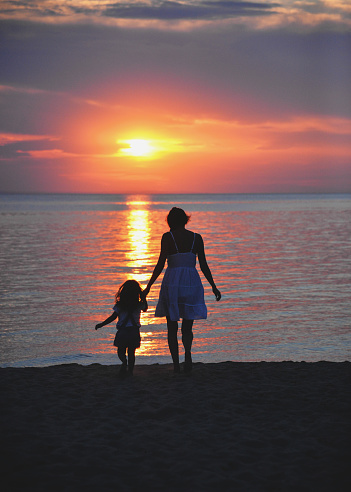 Mother and little daughter walking on beach at sunset