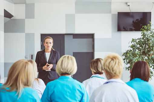 Woman giving a speech on seminar for medical staff. Group of women sitting in a conference room and listening to female speaker.