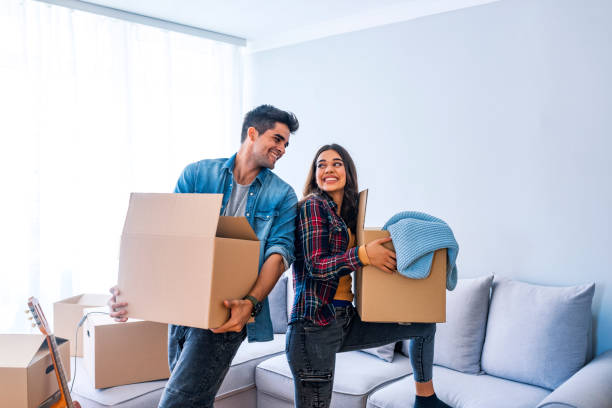 New Home Young couple just moved into new empty apartment unpacking and cleaning - relocation. Young couple carrying big cardboard box at new home.Moving house. show home stock pictures, royalty-free photos & images