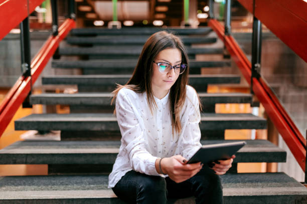 istock Young serious beautiful female teacher sitting on the stairs and using tablet while waiting for class to begin. 1095334656