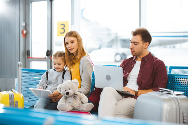 istock cute kid looking at digital tablet near mother while father using laptop in airport 1095344792