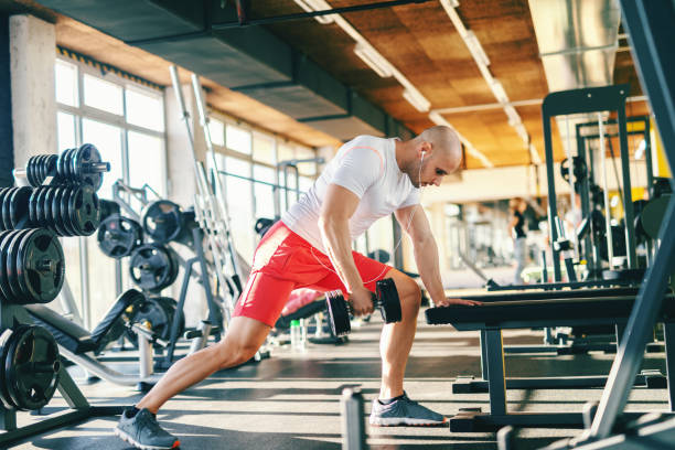 istock Bald Caucasian bodybuilder lifting dumbbells while leaning on the bench. In ears earphones. 1095352796