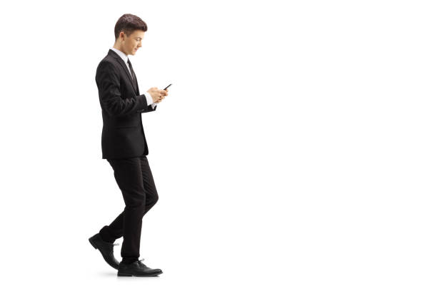 istock Young man in a black suit walking and typing onto a mobile phone 1095367566