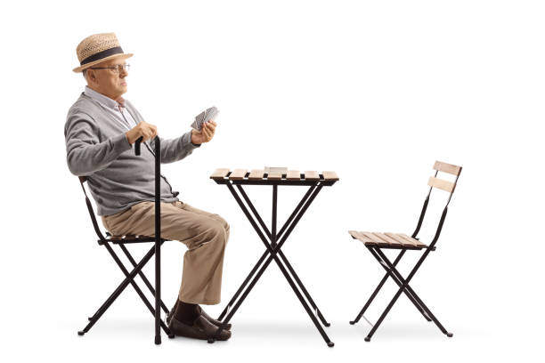 istock Senior man with a cane sitting at a table and playing cards 1095367962