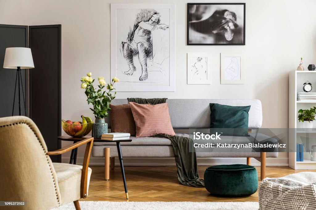 Flowers on wooden table in front of settee under posters in flat interior with armchair. Real photo Sofa Stock Photo
