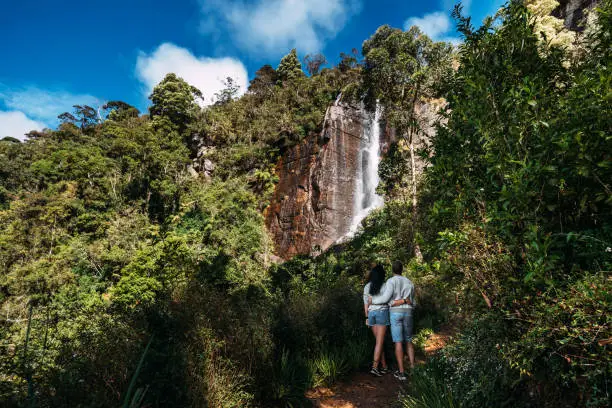 Photo of Couple admires a beautiful waterfall. Couple in love at the waterfall. Boy and girl at the falls. A guy and a girl traveling. The couple travels around Asia. Waterfalls in Sri Lanka. Honeymoon trip