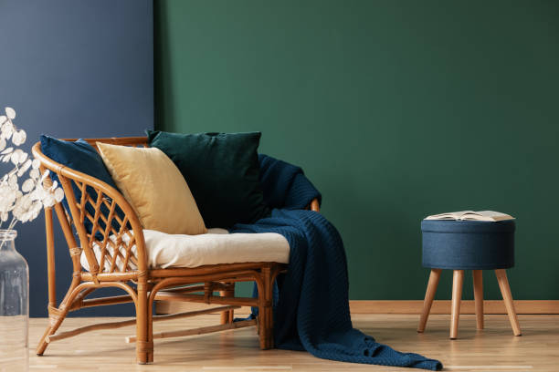 istock Dark blue pouf with open book next to rattan settee with pillows and blanket, copy space on the empty and blue grey wall 1095383044
