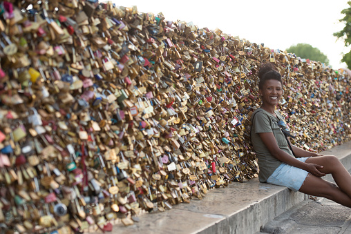 Ethiopian tourist woman sitting on curbstone against Love Locks fence. The famous place in Paris.