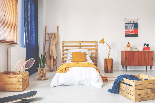 ベッド、木製の箱、バドミントン ラケット、黄色の枕と流行に敏感な寝室のインテリアの本物の写真 - head rest ストックフォトと画像