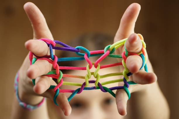 Child playing classic, old-school string game and didactic toy with her fingers, shaping butterfly, developing her motor skills. IQ, education, intelligence, fun and childhood concept.