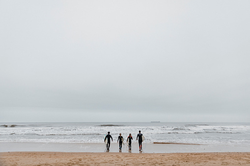 Small group of friends walking towards the water on the beach with their surfboards.