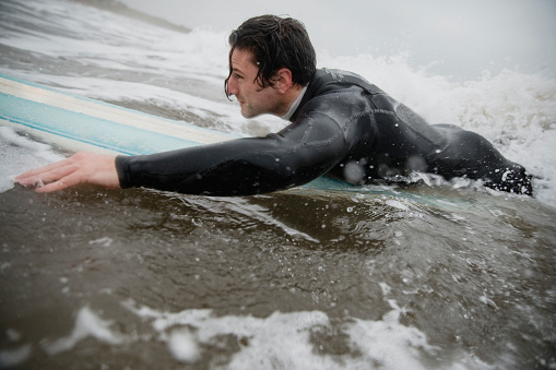 Mid adult man paddling on a surfboard before catching a wave.