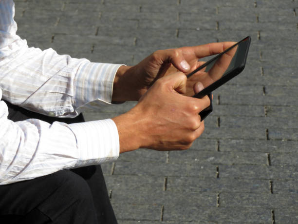 digital-tablette in männlichen händen nahaufnahme, mann im büro anzug sitzt auf der straße mit tablet-pc - sleaze stock-fotos und bilder