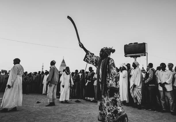 Omdurman, Sudan – December 7, 2018: Highlight of visiting Sudan would be this Sufis ritual as well as Pyramids. Sufis gather every Friday at Hamed al-Nil Tomb in Omdurman, which is a short drive from capital of Sudan, Khartoum. Tons of Sufis start marching around sunset with sticks and flags respectively. As far as I could see, it was only men. Tourist can go watch this ceremony with no issue. After they make a huge circle in front of the mosque, ceremony finally starts. As their chant grows louder, everybody starts moving his body to the chanting happily and clap. They are not in trance but just enjoy the ceremony. Some lead the ceremony with loud voice in the center of the circle, others swirl. Most dervishes wear white thobe but some wear very outstanding costume, which are very colourful and unique patchwork gown or animal printed robe. Surprisingly those who are in outstanding costume have dreadlocks hair !