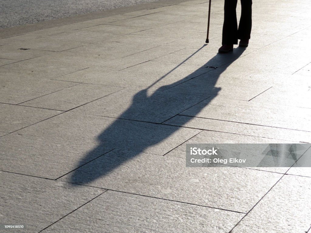 Silhouette and shadow of woman walking with a cane Concept of blind person, disability, old age, diseases of the spine, stranger Loneliness Stock Photo