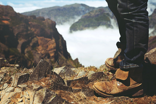 Traveler resting man hipster hiking boots Standing on a high mountain peak having enjoying wonderful breathtaking the forest mountain rocks view. Freedom travel concept. hiking shoes and man legs.
