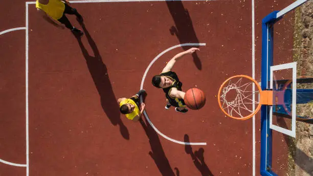 Basketball player scoring with slam dunk, drone point of view, outdoor