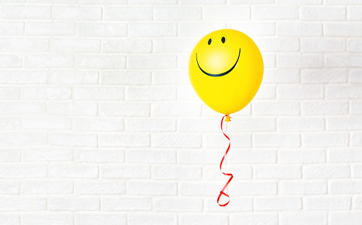 Yellow ballon with smile flying aganst white wall. Copy space