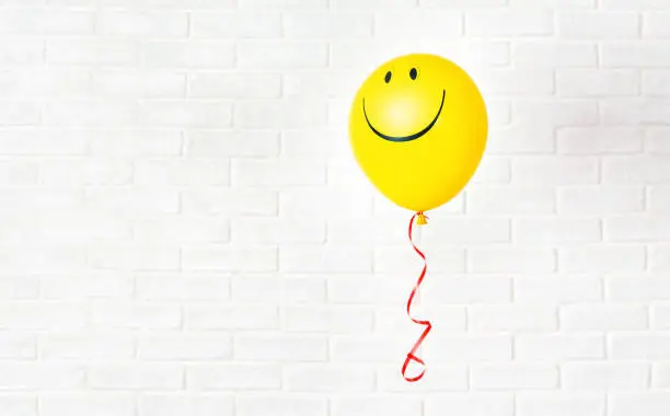 Photo of Yellow ballon with smile hangs aganst white wall