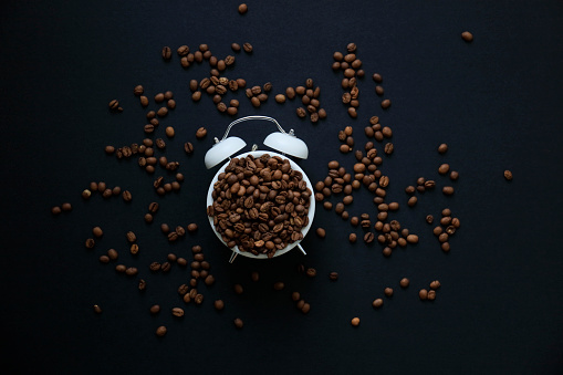 Roasted coffee beans lie all over the frame on a surface with a mottled gray texture. There is space for text in the center of the frame. View from above