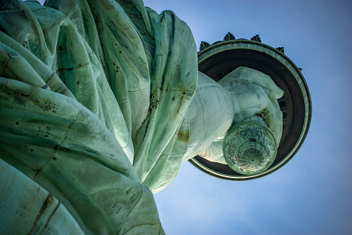 Shot at an unusual angle from below, this image of the Statue of Liberty shows the detail on the base of her torch, which would probably usually go unnoticed. Shot on a beautiful sunny day against a rich blue sky.